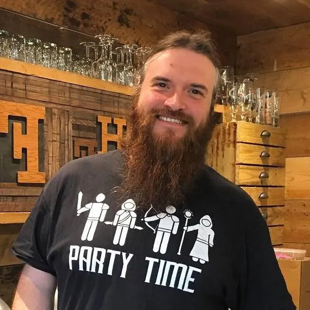 Screaming Cloud standing in a wooden bar and wearing a t-shirt that says Party Time on it with stick figures of an adventuring party
